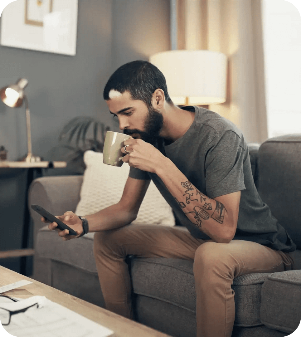 Man sitter hemma med mobiltelefon och kaffekopp